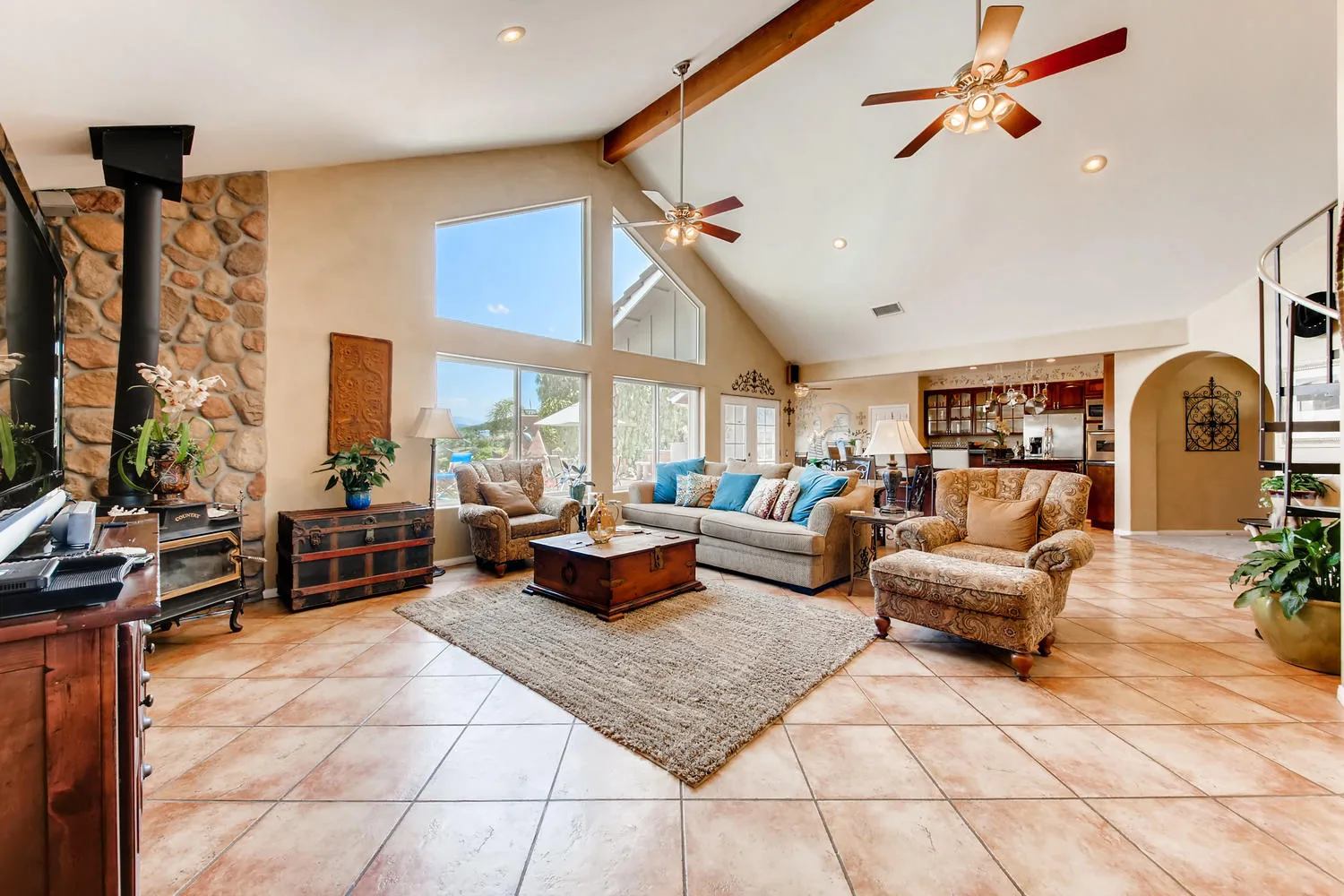 The great room under a sixteen-foot vaulted ceiling with exposed wood beams and a full-height stone chimney